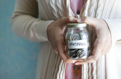 Close up shot of a woman holding a glass jar of various coins with a label on it that says "Savings"