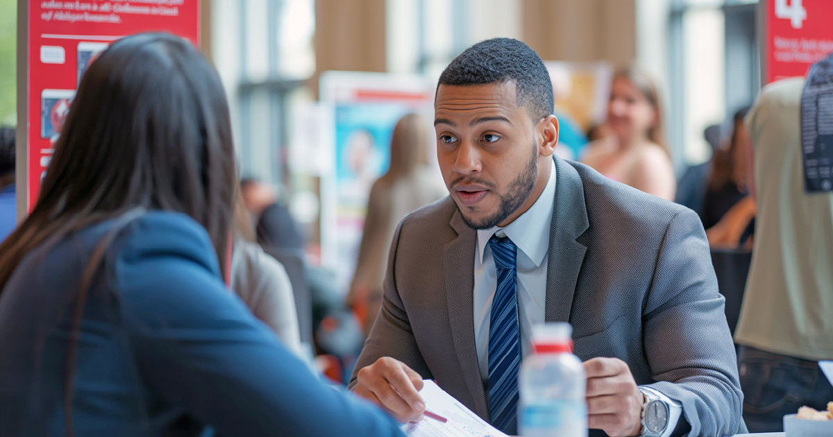 Two people talking to each other across a table at a job fair. 