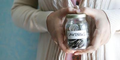 Close up shot of a woman holding a glass jar of various coins with a label on it that says "Savings"
