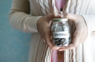 Close up shot of a woman holding a glass jar of various coins with a label on it that says "Savings"