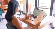 A person working on a laptop and holding sheets of paper in her right hand.