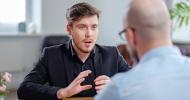 Two people having a conversation as they sit across a desk from each other during a job interview.